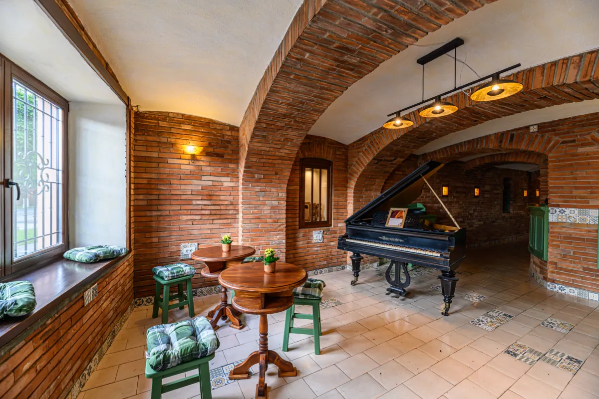 Interiorul Hanului Bucuriei, cu arcade de cărămidă, pian cu coadă și lămpi calde aprinse.